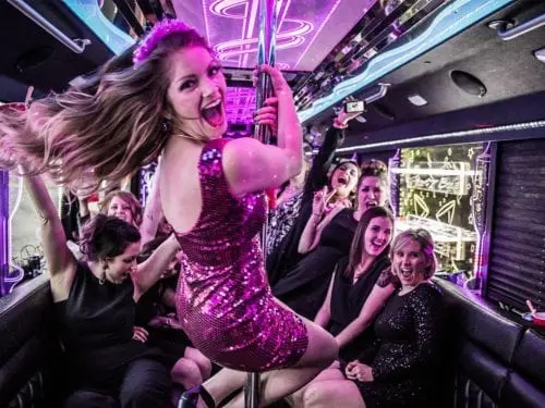 Woman dancing on a pole inside a party bus with excited passengers.
